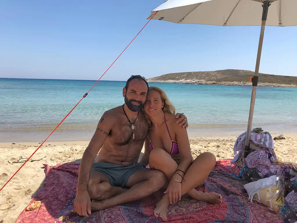 Vasken and Eva on a sandy paradise beach in Antiparos under the shade of a beach umbrella.